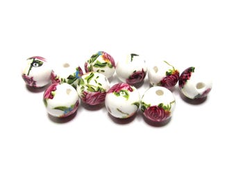 May include: A collection of white ceramic beads with floral designs. The beads feature red, pink, green, and blue painted flowers. Each bead has a hole for stringing.