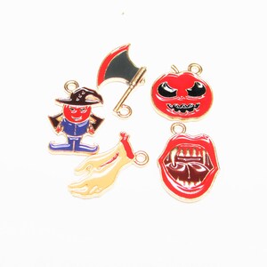 May include: Six gold-tone metal Halloween charms with red, black, and white enamel paint. The charms include a pumpkin, a vampire mouth, a bloody hand, an axe, and a witch.