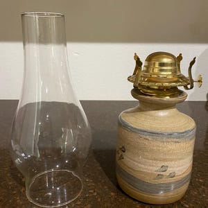 Puede incluir: Una lámpara de aceite de cerámica con un esmalte azul y marrón. La lámpara tiene un portamechas de latón y una chimenea de vidrio transparente.