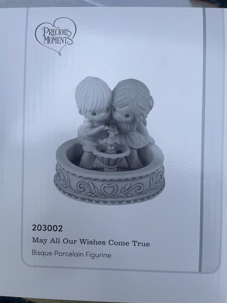 May include: A bisque porcelain figurine depicting two figures embracing near a fountain. The base is decorated with heart-shaped designs. The text reads "May All Our Wishes Come True."
