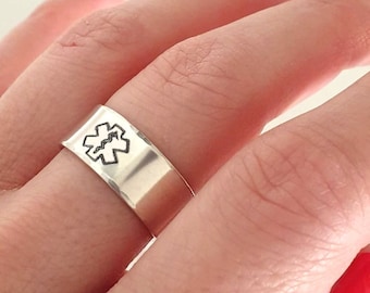 May include: A silver ring with a medical symbol engraved on it. The ring is worn on a finger with red nail polish.