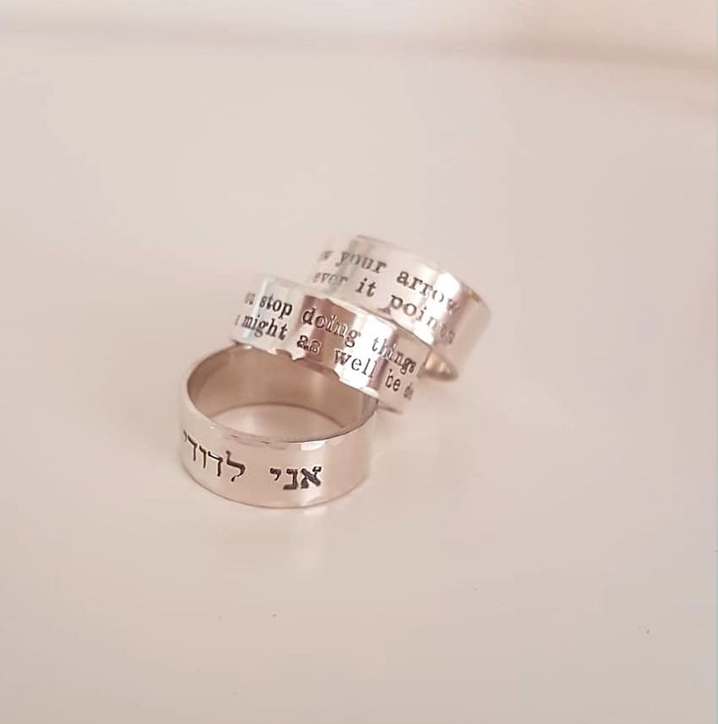 May include: Three silver rings with engraved text. The top ring reads "If your arrows never point", the middle ring reads "You stop doing things I might as well be d", and the bottom ring reads "אך לזה" in Hebrew.