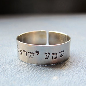 May include: A silver ring with the Hebrew words "Shema Yisrael" engraved on it.