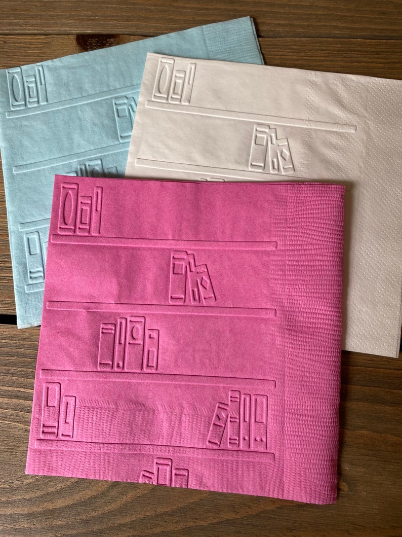 May include: Three paper napkins with a bookshelf design. The napkins are in blue, white, and pink.