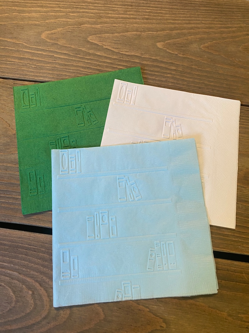 May include: Three paper napkins with a bookshelf design. The napkins are green, white, and light blue.