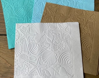 May include: Four paper napkins with an embossed seashell and starfish design. The napkins are in shades of blue, brown, and white.