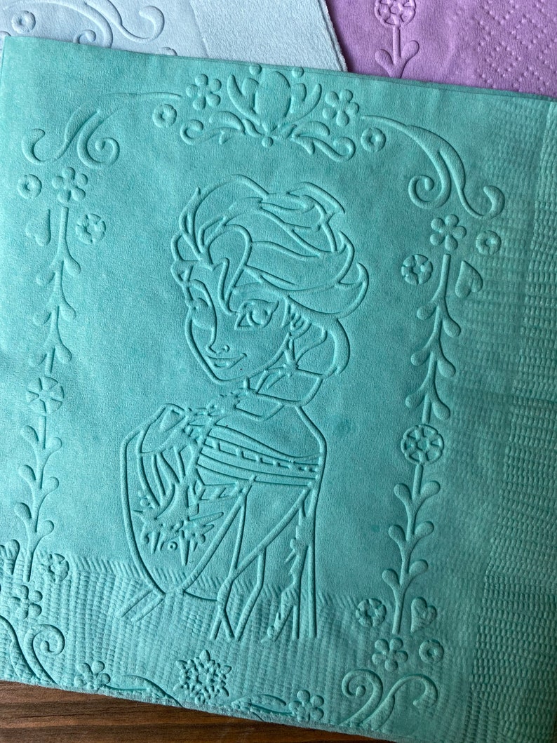 May include: A teal blue kitchen towel with an embossed design of a cartoon character with long blonde hair. The character is wearing a blue dress and has a floral design around the border.