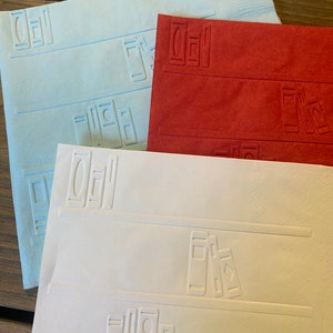 May include: Three decorative paper placemats with an embossed design of books on a bookshelf. The placemats are in blue, red, and white.