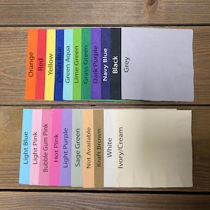 May include: A color chart of paper samples for crafting and scrapbooking. The colors include orange, red, yellow, cobalt blue, green aqua, lime green, grass green, dark purple, navy blue, black, grey, light blue, light pink, bubble gum pink, hot pink, light purple, sage green, not available, kraft brown, white, and ivory/cream.
