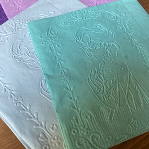 May include: Four paper napkins with an embossed floral design. The top napkin is green and features a silhouette of a person with a crown. The other napkins are light blue and purple.
