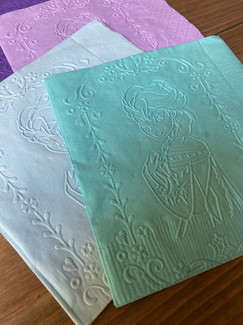 May include: Four paper napkins with an embossed floral design. The top napkin is green and features a silhouette of a person with a crown. The other napkins are light blue and purple.