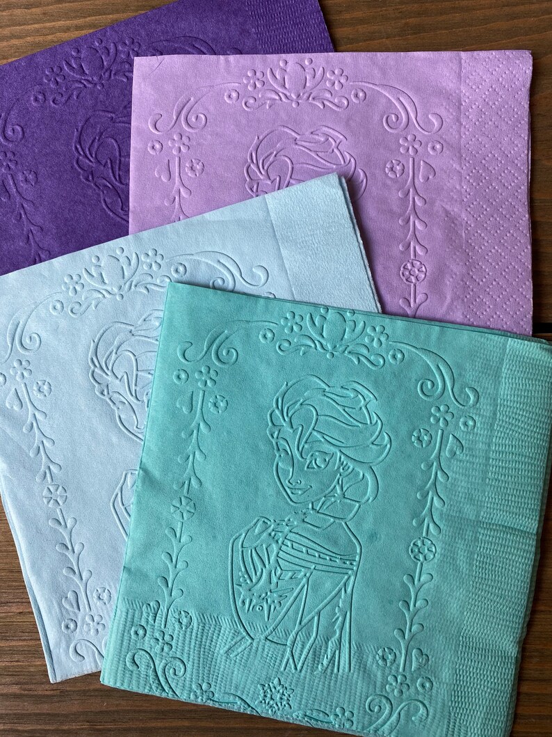 May include: Four paper napkins with an embossed design. The napkins are in shades of purple, light blue, and green. The green napkin features an embossed image of a woman with long hair and a crown.