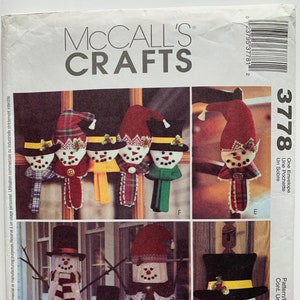 May include: A sewing pattern for making snowman decorations. The pattern includes instructions for making five different snowmen, including a large snowman with a hat and scarf, a smaller snowman with a hat and scarf, and a snowman head with a hat and scarf. The pattern also includes instructions for making a snowman envelope and a snowman pouch.