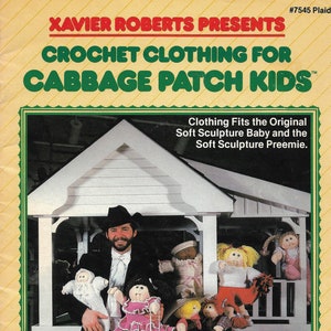 May include: A book cover featuring a man in a suit holding Cabbage Patch Kids dolls. The cover reads "Xavier Roberts Presents Crochet Clothing for Cabbage Patch Kids." The book is for crocheting clothing for Cabbage Patch Kids dolls.
