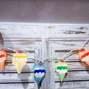 May include: A string of decorative lights featuring colorful ice cream cone shapes. Each cone has a different color of ice cream and a red cherry on top. The lights are strung on a white wire, perfect for a party or room decor.