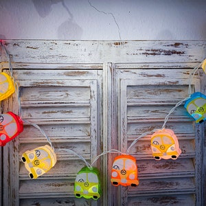 May include: A string of colorful lights shaped like vintage vans with peace signs. The lights are strung across a white wooden shutter.
