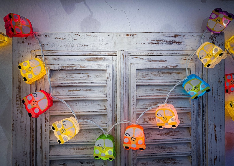 May include: A string of colorful lights shaped like vintage vans with peace signs. The lights are strung across a white wooden shutter.