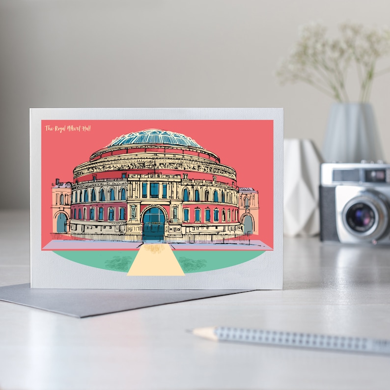 Pu&ograve; includere: Biglietto di auguri con una colorata illustrazione della Royal Albert Hall. L'edificio iconico &egrave; raffigurato in rosso, beige e blu su uno sfondo rosso. Il testo "The Royal Albert Hall" &egrave; visualizzato in alto.