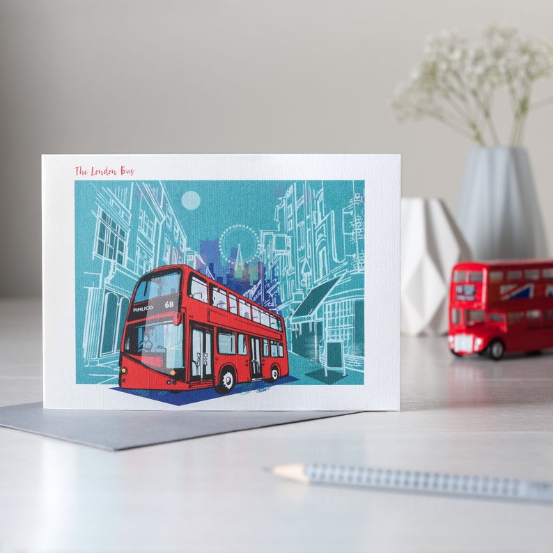 Puede incluir: Una tarjeta de felicitaci&oacute;n con una ilustraci&oacute;n de un autob&uacute;s londinense de dos pisos rojo sobre un fondo turquesa con dibujos de edificios en blanco. El texto "The London Bus" est&aacute; en la parte superior izquierda. Un peque&ntilde;o modelo de autob&uacute;s rojo est&aacute; en el fondo.