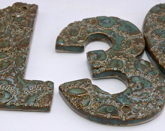 May include: Three ceramic house numbers, 1, 3, and 0, in a green and brown glaze with a decorative pattern. The numbers are individually crafted and have a rustic, handmade look.