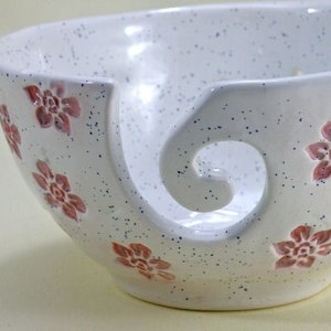 May include: White ceramic yarn bowl with a pink floral design and a large, curved opening for yarn.