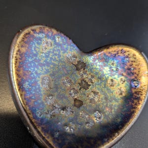 Puede incluir: Un juego de tres tazas de cerámica con un esmalte moteado de color crema. Cada taza presenta un diseño pintado a mano diferente: un sol, una luna y una estrella. Las tazas tienen un diseño simple y moderno con forma redondeada.