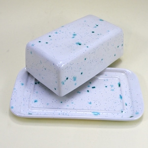 May include: White ceramic butter dish with a blue speckled design. The dish has a lid and a base.