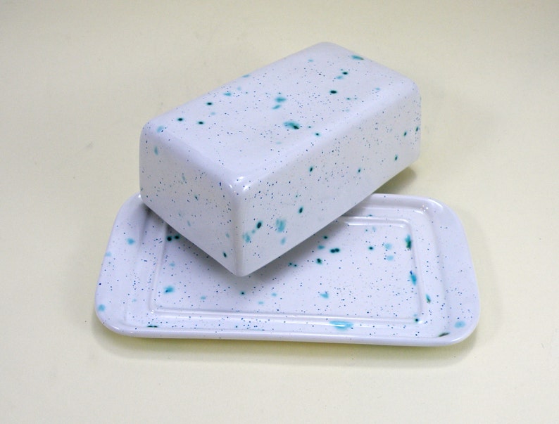 May include: White ceramic butter dish with a blue speckled design. The dish has a lid and a base.