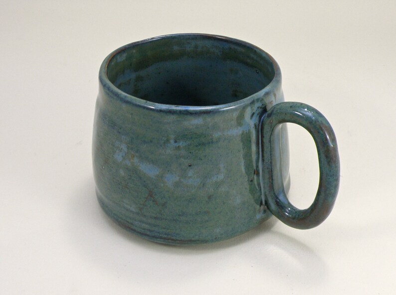 May include: A teal blue ceramic mug with a rounded body and a slightly flared rim. The mug has a handle that is attached to the side of the mug.