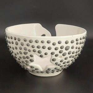 May include: White ceramic bowl with a star-shaped cutout and a textured surface of small gray dots.
