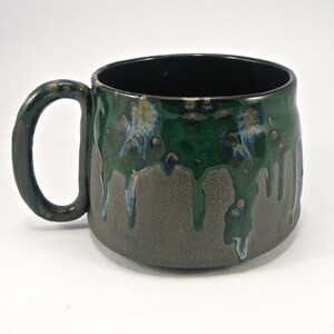 May include: A green and brown ceramic mug with a drip glaze design. The mug has a wide, rounded body and a handle.