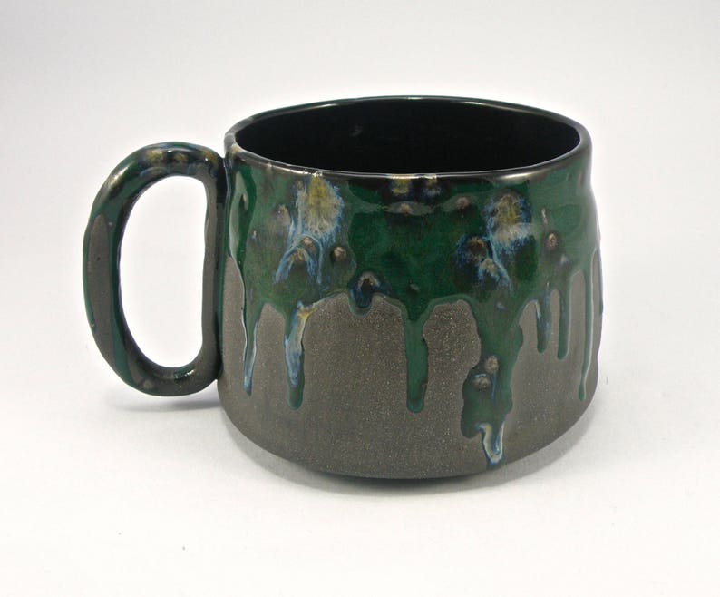 May include: A green and brown ceramic mug with a drip glaze design. The mug has a wide, rounded body and a handle.