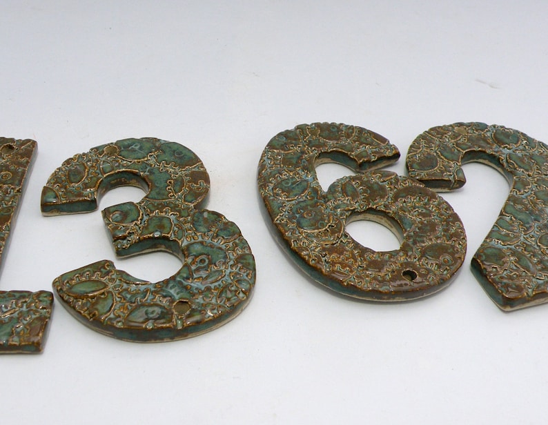 May include: Ceramic house numbers in a green and brown glaze with a decorative pattern. The numbers are 1, 3, 6, and 2.