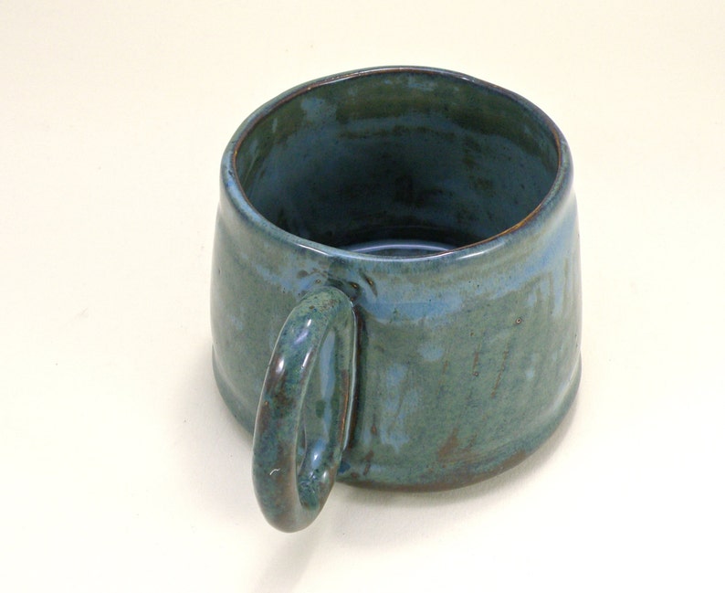 May include: A handmade ceramic mug with a teal glaze and a brown handle. The mug has a rustic, handmade look.