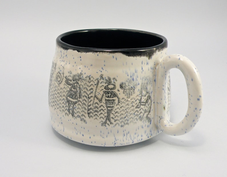 May include: White ceramic mug with a black rim and a design of stylized figures in black on the side. The mug has a speckled glaze.