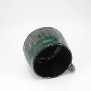 May include: A green and black ceramic mug with a drip glaze design. The mug has a rounded shape and a handle.