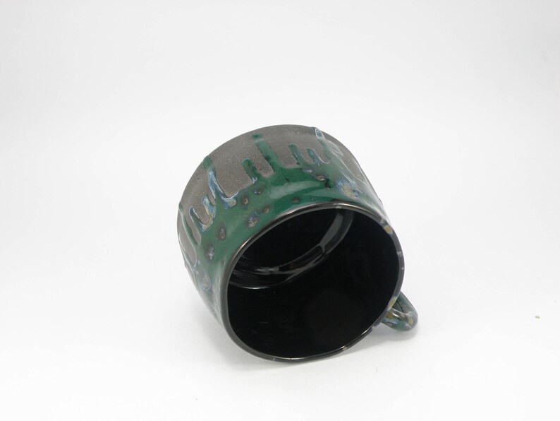 May include: A green and black ceramic mug with a drip glaze design. The mug has a rounded shape and a handle.