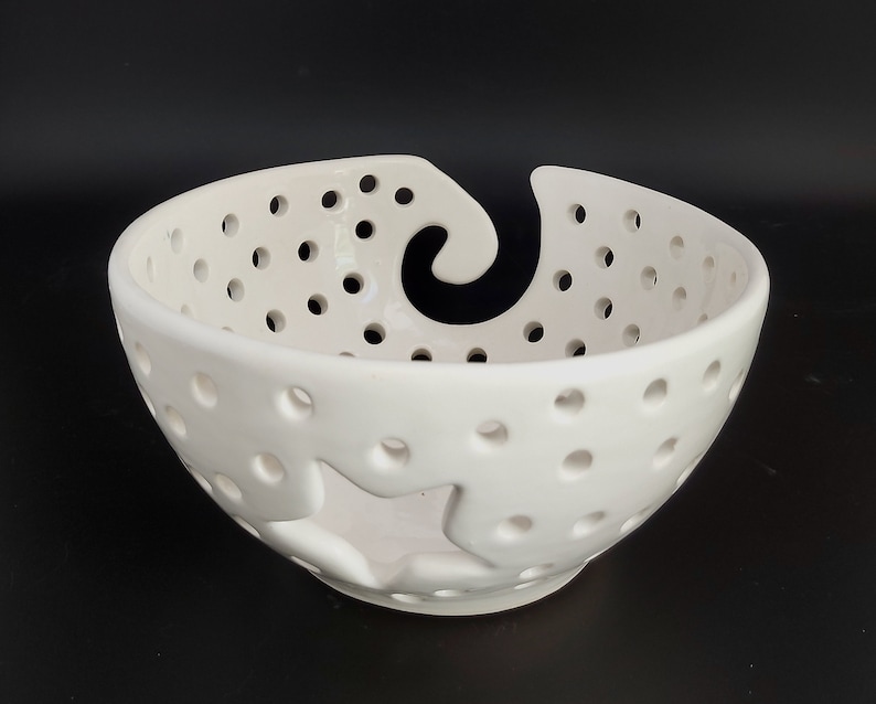 May include: White ceramic bowl with a star-shaped cutout and a swirl design. The bowl has small holes throughout the surface.