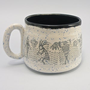 May include: White ceramic mug with a black rim and a blue and black design of stylized figures. The mug has a speckled blue glaze.