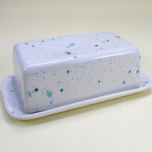 May include: White ceramic butter dish with a speckled green and blue glaze. The dish has a rectangular shape and a matching lid.