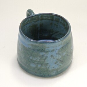 May include: A blue ceramic mug with a speckled glaze. The mug has a rounded shape and a handle.