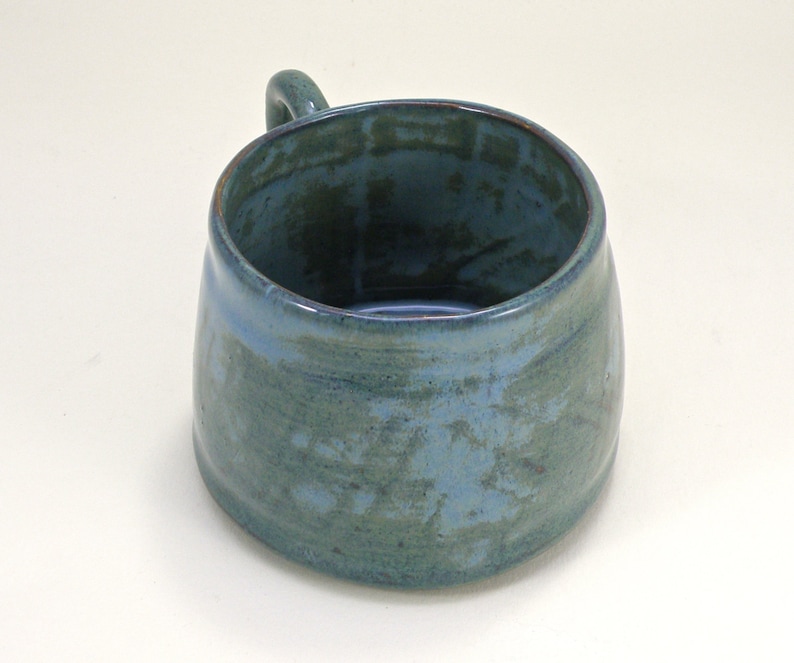 May include: A blue ceramic mug with a speckled glaze. The mug has a rounded shape and a handle.
