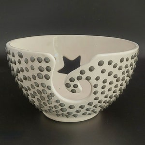 May include: White ceramic yarn bowl with a star and a swirl design. The bowl is covered in small gray dots.
