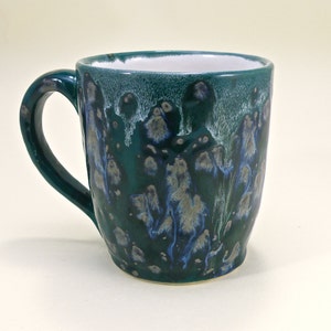 May include: A green ceramic mug with a white handle and blue and white speckles throughout.