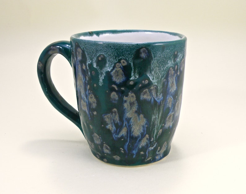 May include: A green ceramic mug with a white handle and blue and white speckles throughout.