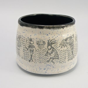 May include: White ceramic bowl with a black rim and a speckled glaze. The bowl features a black and white design of stylized figures and a rain cloud.