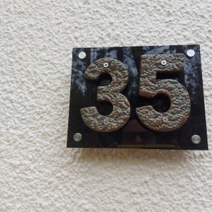 May include: A black plaque with a reflective surface displays the number 35 in large, brown, textured numerals. The numerals are attached to the plaque with silver screws.