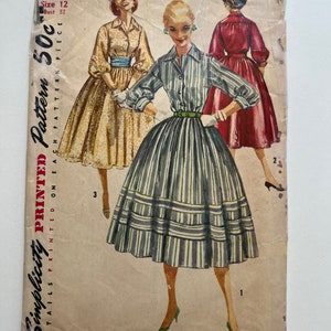 May include: Vintage Simplicity sewing pattern for a dress, size 12, bust 32. The pattern is printed on a tan paper with a red and white border. The pattern shows a woman wearing a striped dress with a green belt and a white collar.