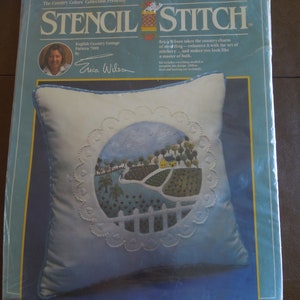 May include: A packaged Stencil Stitch kit featuring an English Country Cottage design. The pillow kit includes a pillow with a blue border and a central design of a cottage, trees, and a white picket fence. The package includes text by Erica Wilson.