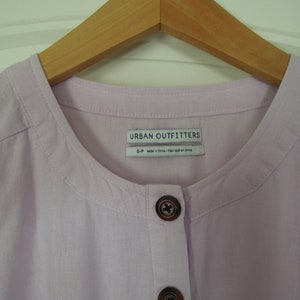 May include: A light purple button-up shirt with a round collar and a label that reads "Urban Outfitters".